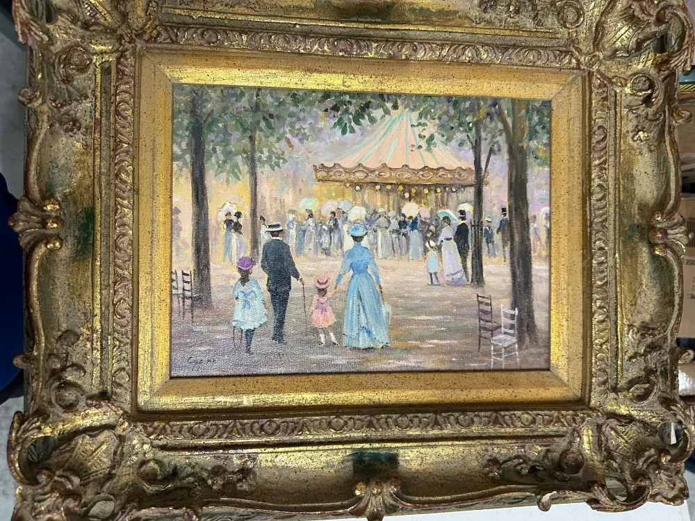 Colorful framed street scene depicting finely dressed figures near an outdoor pavilion or café in an elaborate gilt frame.