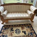 Statement sofa with cream tufted upholstery, exposed carved-wood frame, scroll arms, and decorative medallion details.