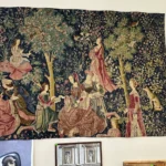 Large wall tapestry depicting figures in elaborate dress gathered beneath trees in a medieval garden scene.