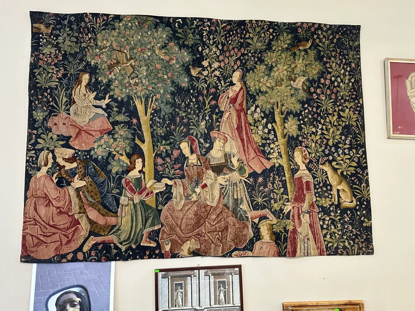 Large wall tapestry depicting figures in elaborate dress gathered beneath trees in a medieval garden scene.