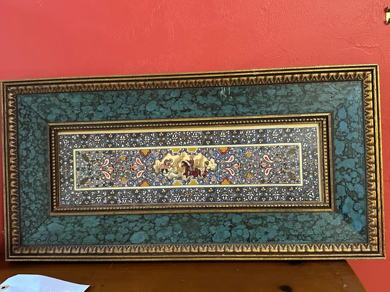 Large decorative textile or tapestry-style panel with intricate floral and geometric borders, mounted in an ornate frame.