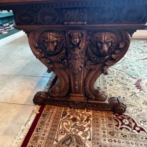 Detail view of a substantial statement table with an elaborately carved pedestal base and carved apron.