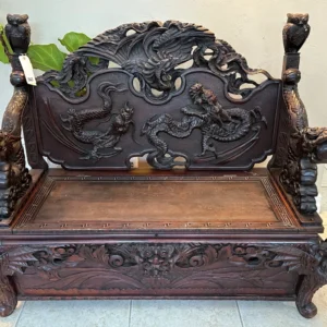 Grand dark-wood bench with extensive relief carving, high decorative back, sculpted arms, and storage-style seat.