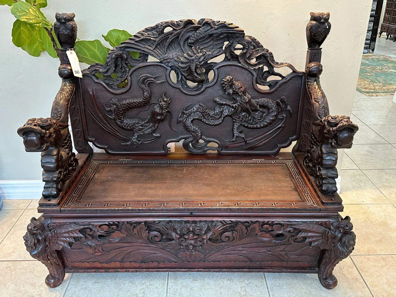 Grand dark-wood bench with extensive relief carving, high decorative back, sculpted arms, and storage-style seat.