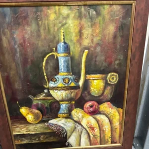 Framed still life featuring a decorative wine vessel, goblets, fruit, and bread against a dark background.